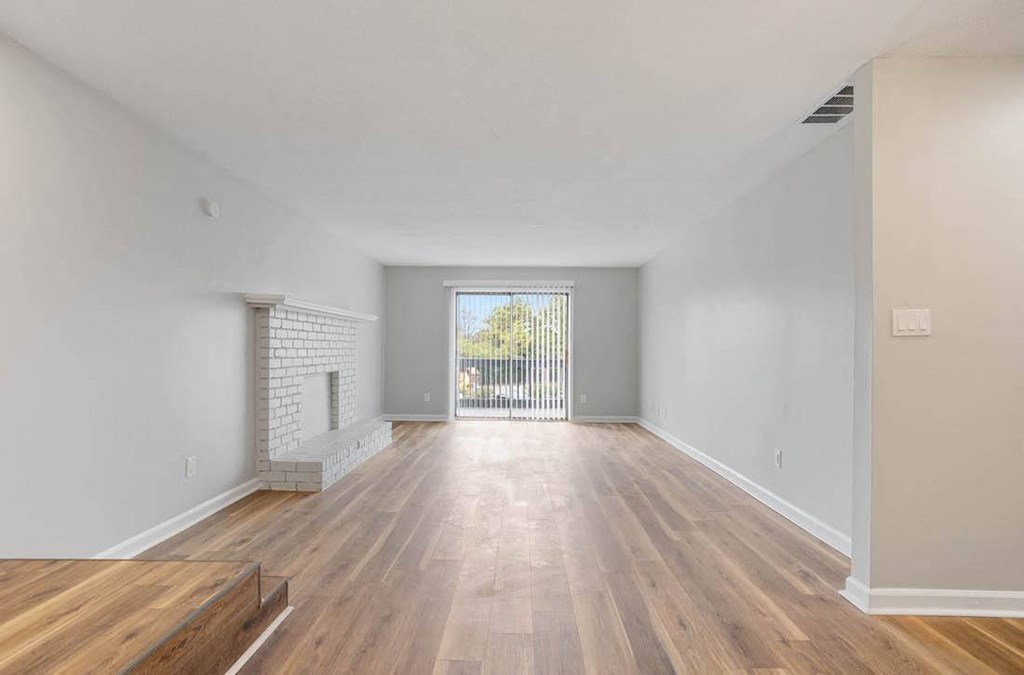 an empty living room with a fireplace and warm hardwood-style floors