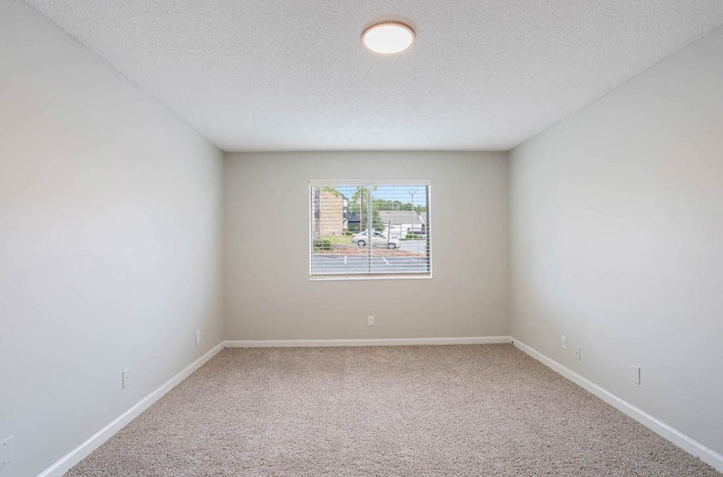 an empty bedroom with a large window, carpet, and overhead lighting