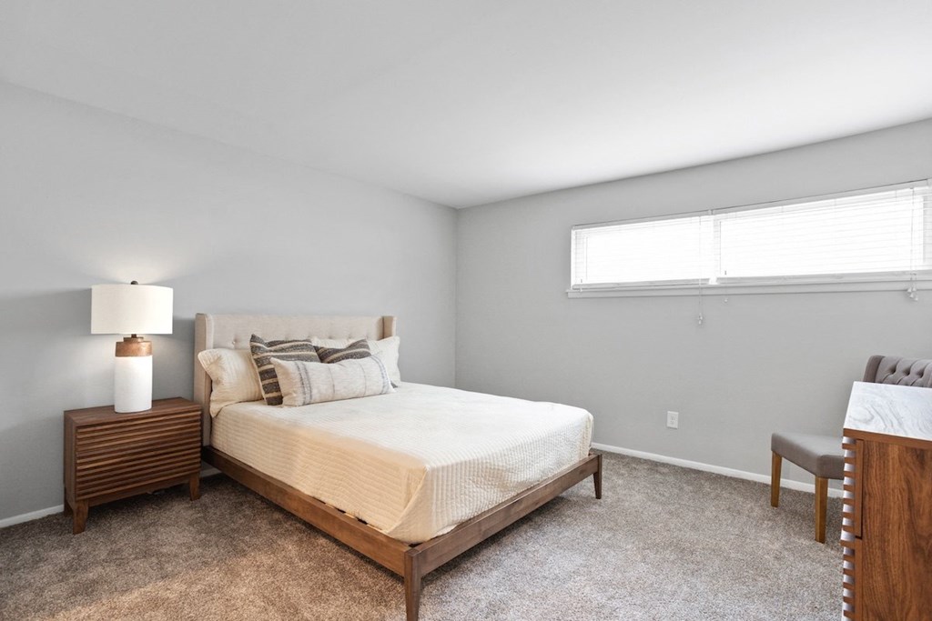 a bedroom with furnishings, a long narrow window, and plush carpeting at Mountainside Apartments