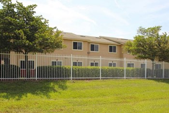 fence surrounding country manor apartments with mature trees and neat grass - Photo Gallery 5