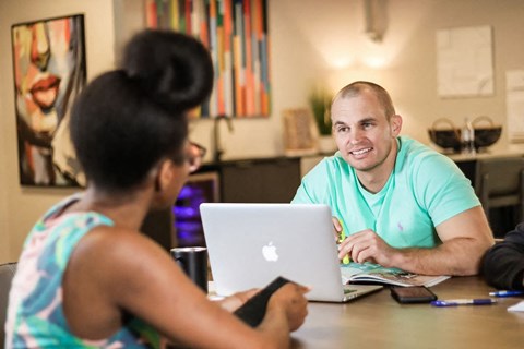 a man and a woman sitting at a table with a laptop in the mezzanine lounge at Citizen