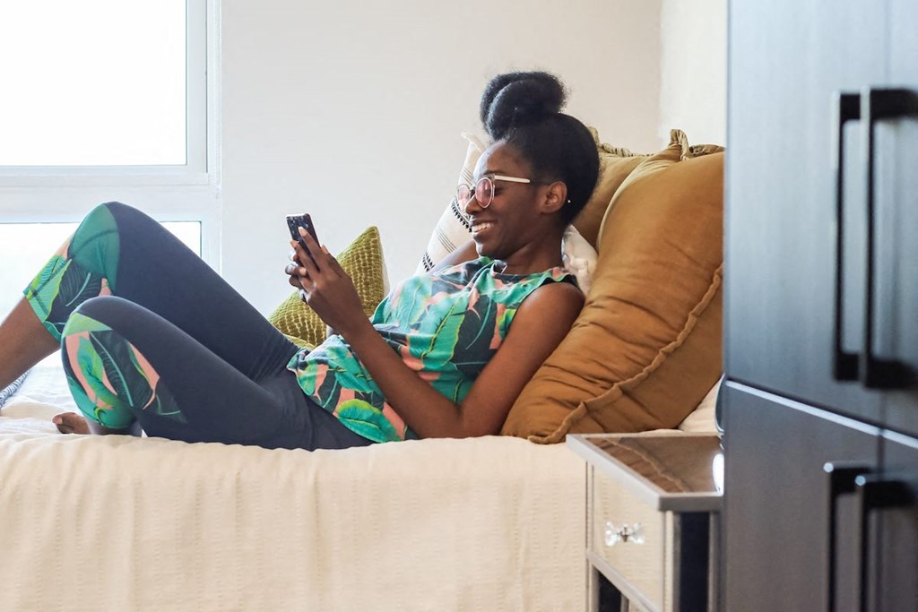 a woman laying on a bed looking at her phone in a Citizen Studio Apartment