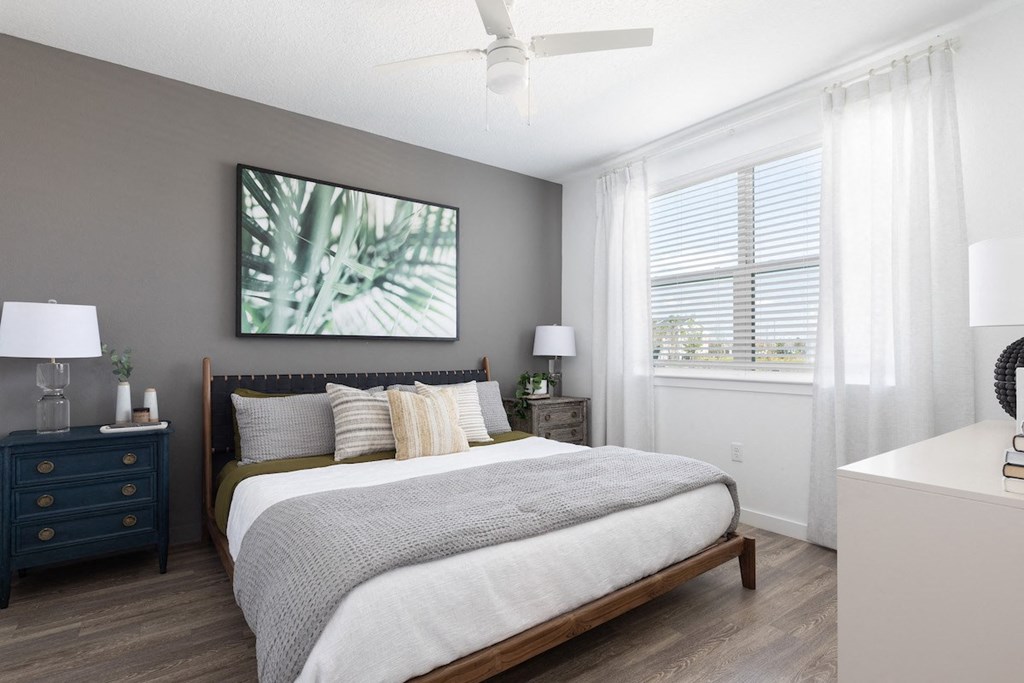 a bedroom with a ceiling fan, large window, wood-style floors, and model furnishings