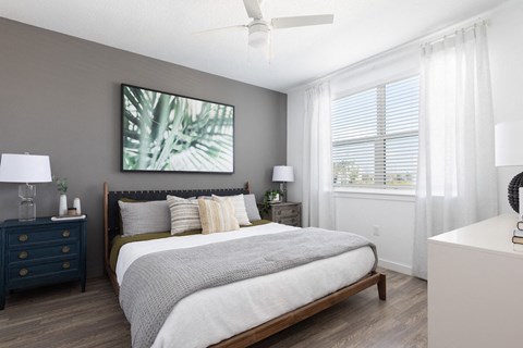 a bedroom with a ceiling fan, large window, wood-style floors, and model furnishings