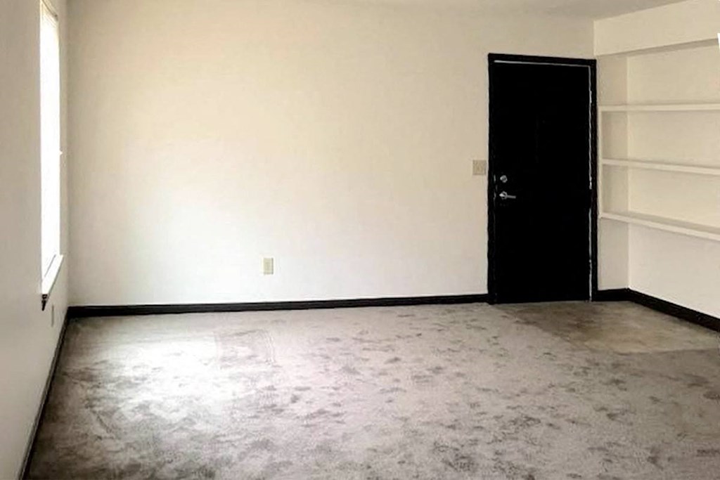 an empty bedroom with built-in shelving, a window, and door