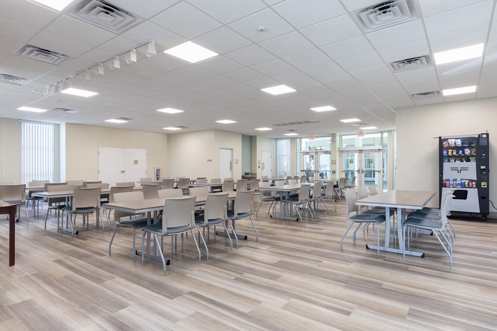 A room with tables and chairs and a vending machine.