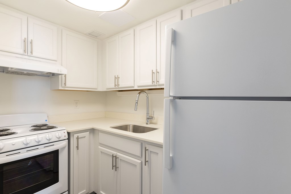 A white kitchen with a refrigerator, oven, and sink.