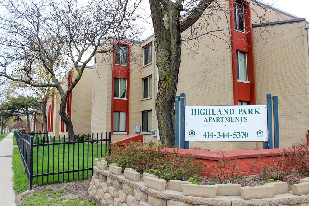 A sign for Highland Park Apartments is in front of a brick building.