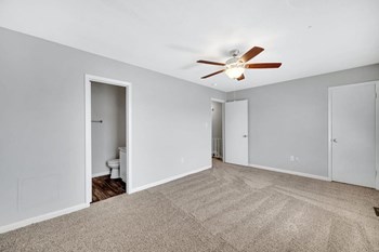large bedroom with illuminated ceiling fan, plush carpet, and attached bathroom at Goshen Estates - Photo Gallery 9