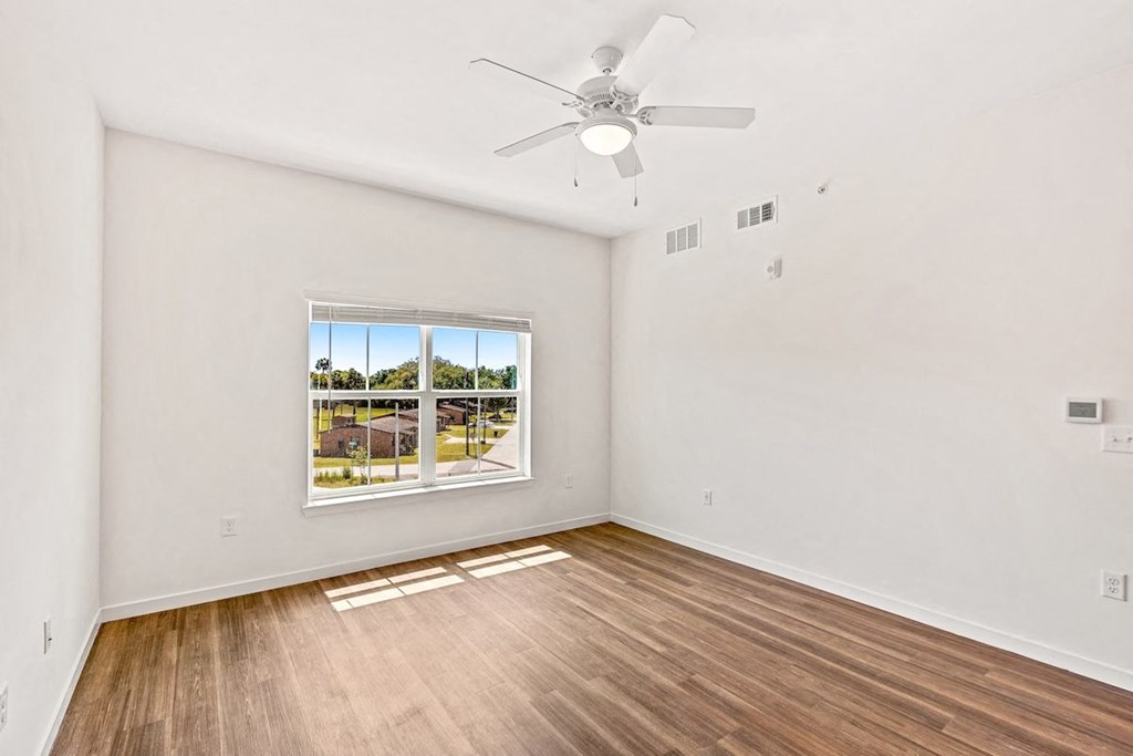 an empty living room with a window and a ceiling fan