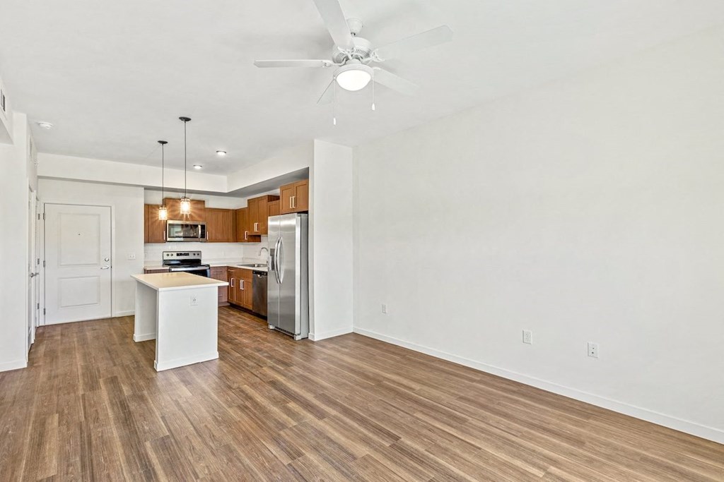 an empty living room with a kitchen and a ceiling fan