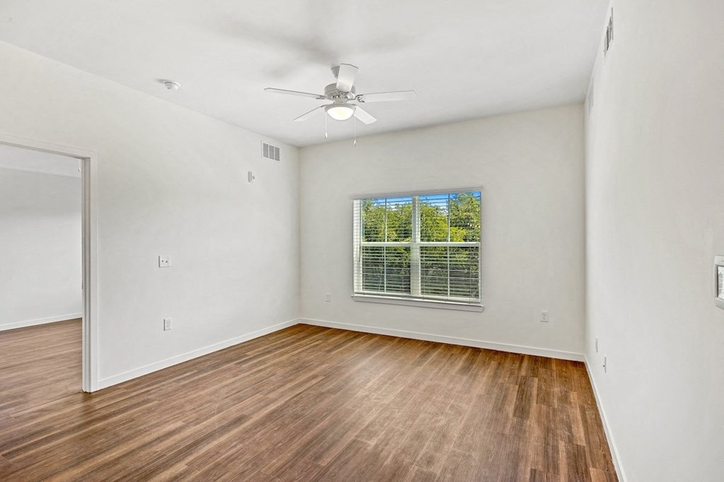 an empty living room with a window and a ceiling fan