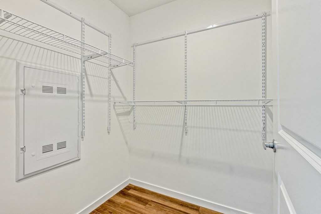 the walk in closet of a bedroom with white walls and shelves and a glass door