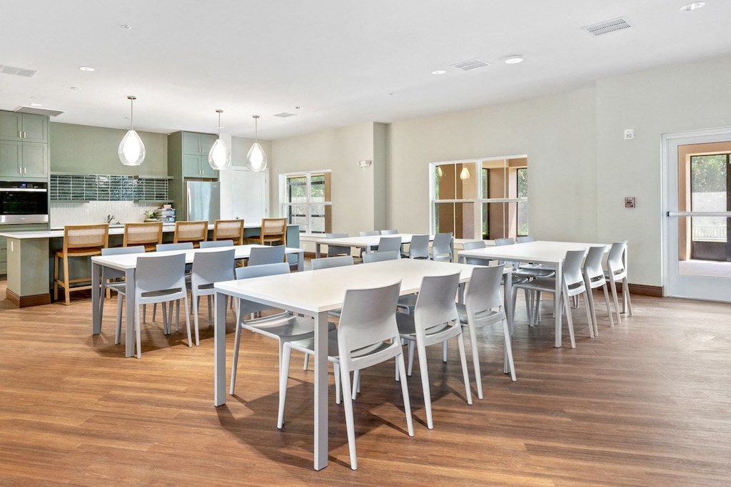 a dining room with white tables and chairs and a kitchen