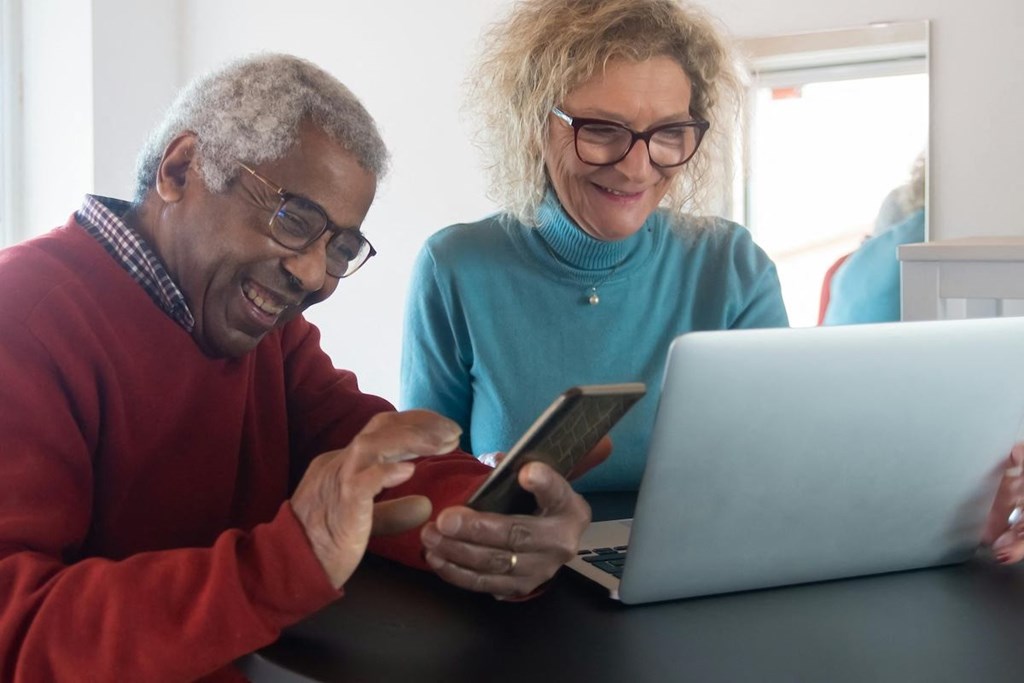 an elderly man and woman looking at a laptop computer and a cell phone