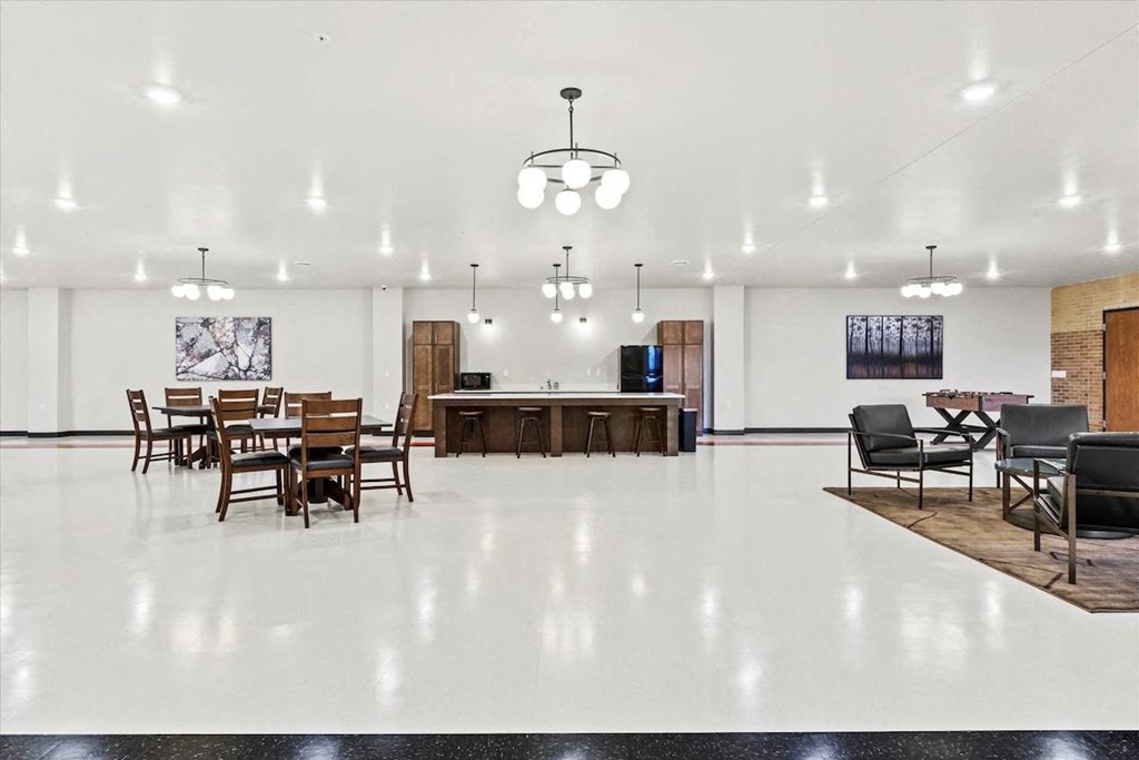 an expansive community room with tables, chairs, a tv, fooseball table and kitchenette at Horicon School Apartments