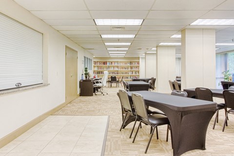 large community room with tables and chairs by computer station & library