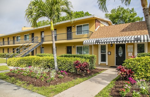 a yellow building with a leasing office and palm trees