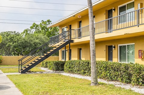 a yellow house with a staircase and a grass yard