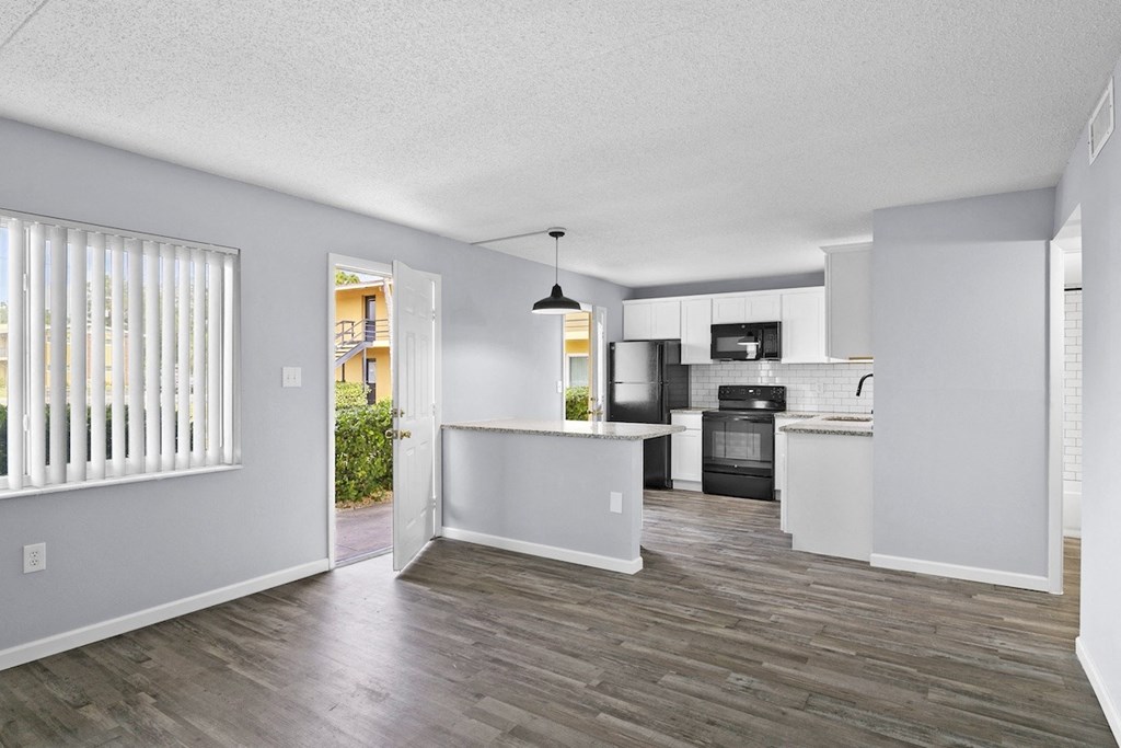 the living room and kitchen of an apartment with white walls and wood floors