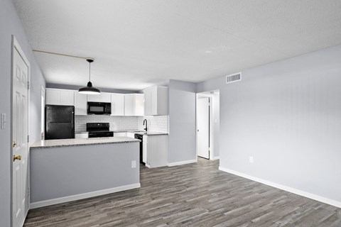 the living room and kitchen of an apartment with white walls and wood flooring