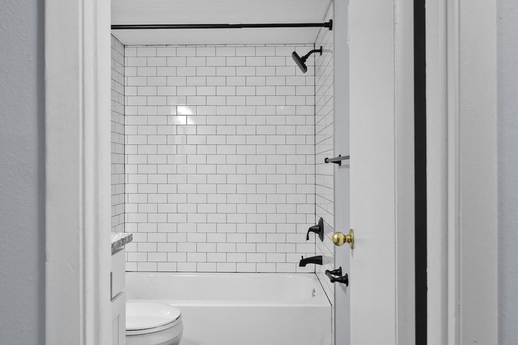 a bathroom with white subway tile and a tub and a toilet
