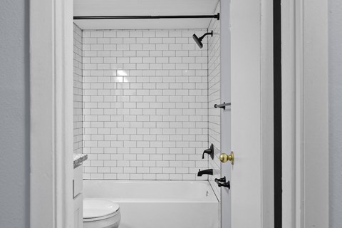 a bathroom with white subway tile and a tub and a toilet