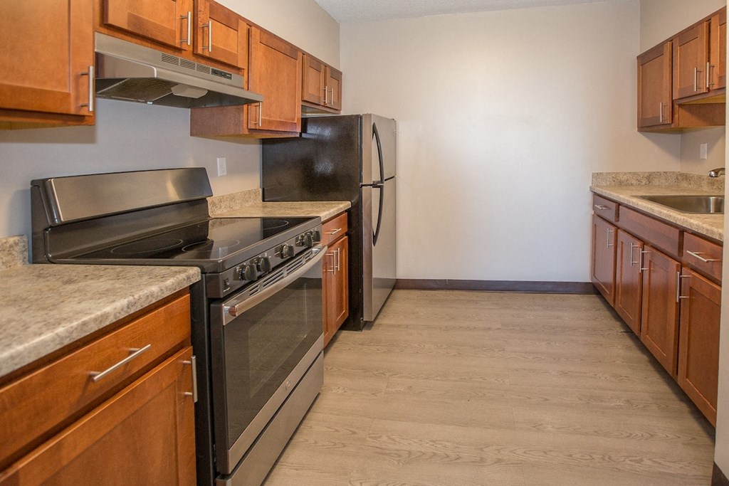 a kitchen with warm wood cabinets, stainless steel appliances, and wood-style flooring at Piotr Stadnitski Gardens senior apartments