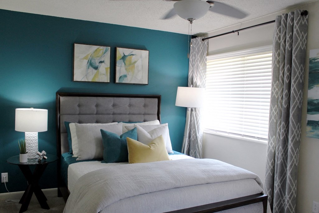 bedroom with large window, modern ceiling fan, teal accent wall and model furnishings  at Huntsville Landing Apartments, Huntsville, Alabama