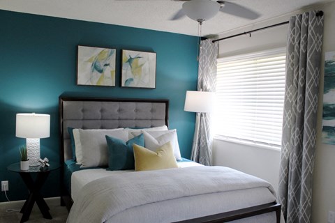bedroom with large window, modern ceiling fan, teal accent wall and model furnishings  at Huntsville Landing Apartments, Huntsville, Alabama