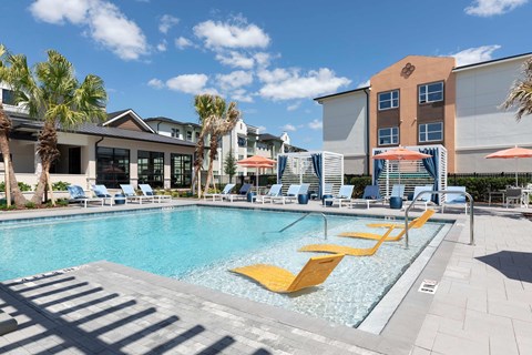A pool with yellow sun loungers and a building in the background.