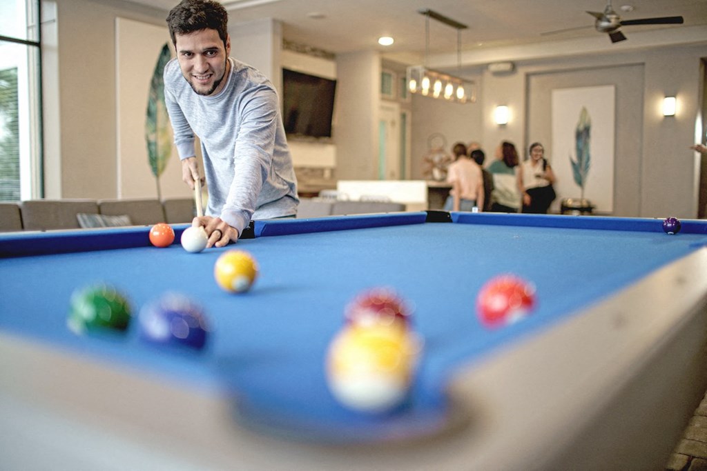 man shooting a pool shot and people behind him hanging out