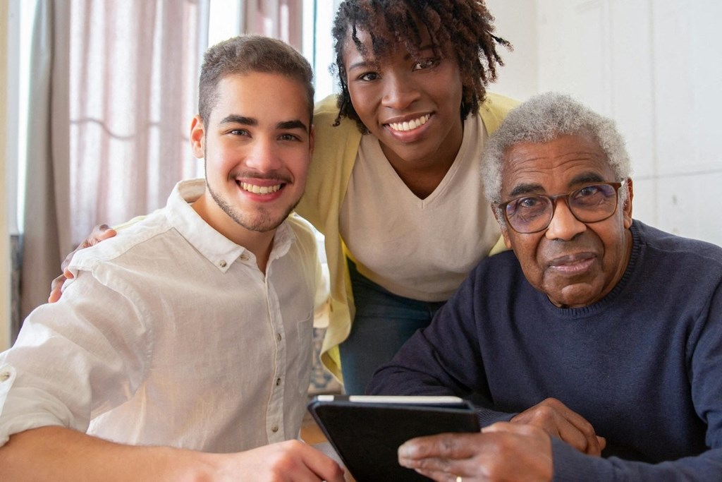 an older man with a tablet and two younger people smiling at the camera