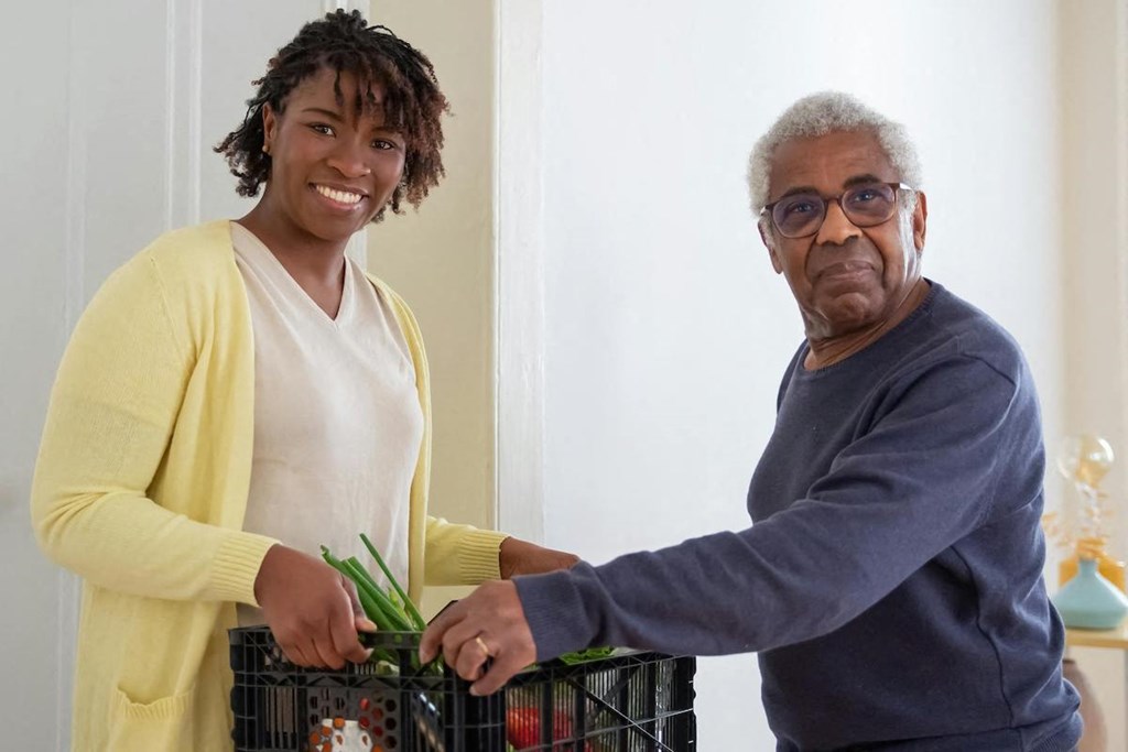 an older man taking a crate of groceries from a younger woman