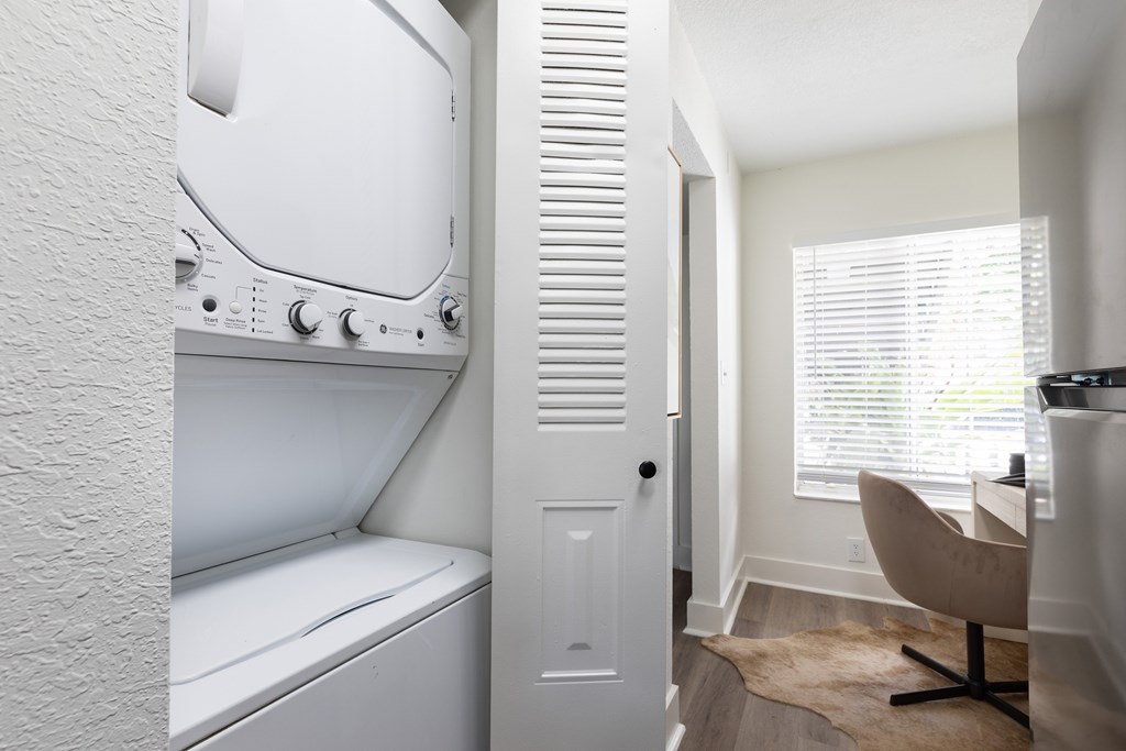 A white washing machine is in a small room with a chair and a rug.