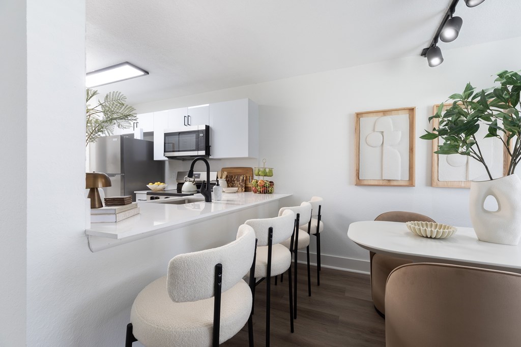 A kitchen with white cabinets and a counter with chairs around it.