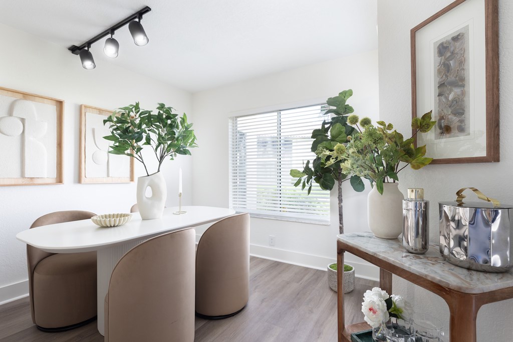 A white table with a bowl of flowers on it and a vase with a green plant.