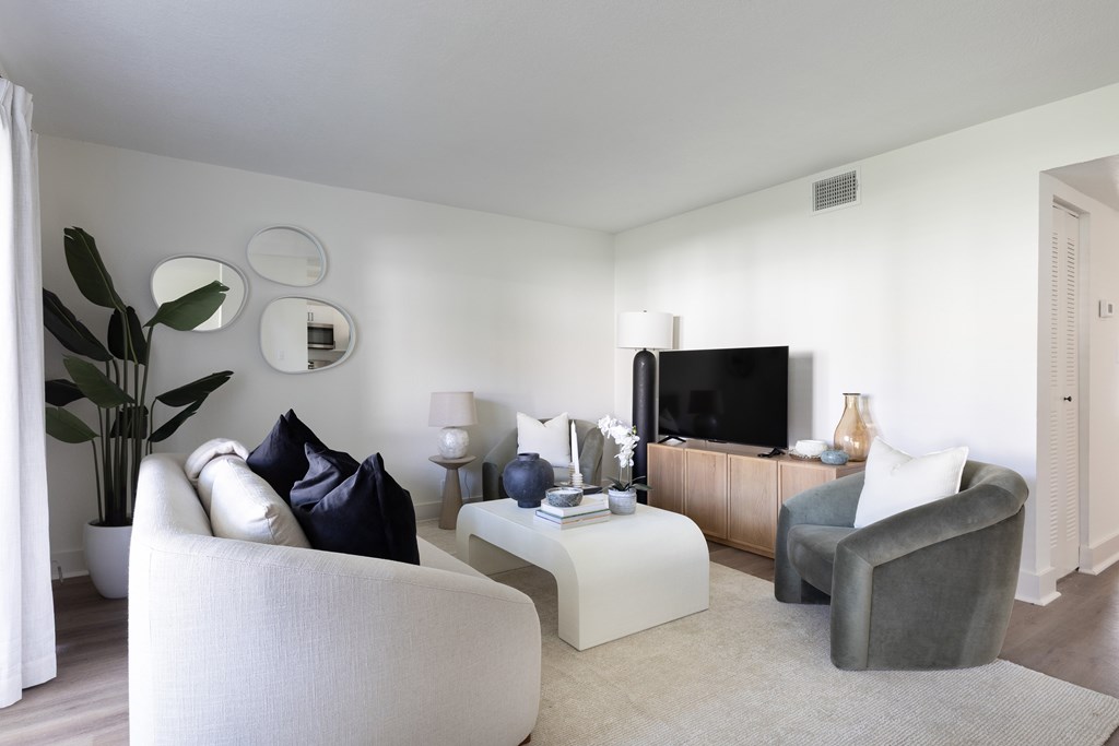 A living room with a white couch, a grey armchair, a white coffee table, a television, and a plant.