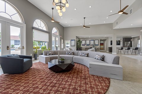 A spacious living room with a grey sofa set and a red patterned rug.