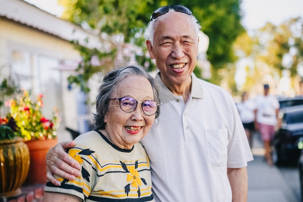 Older couple smiling outide surrounded by flowers and trees