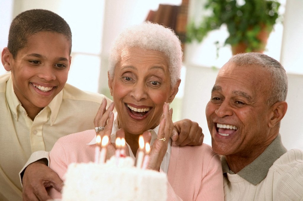 woman being surprised with a birtday cake by a man and boy