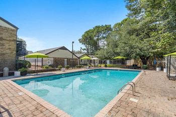 a large rectangular pool and sundeck surrounded by apartments and trees
