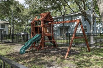 A wooden and plastic playground set with a swing set, slide, and other play features at Terraces at Clearwater Beach