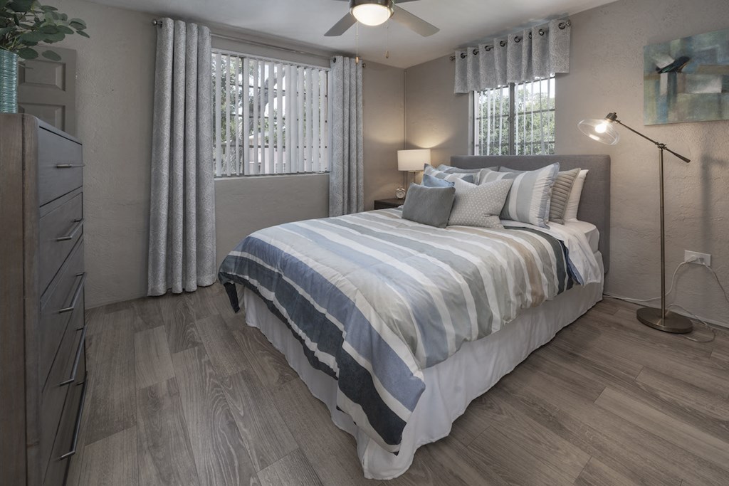 Bedroom with two large windows, fan, wood-style floor, and model furnishings at Terraces at Clearwater Beach, Florida