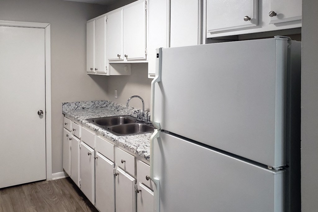 Fridge, white cabinets, and double stainless steel sink in apartment kitchen at The Bluffs