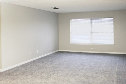 large carpeted living room with a wide window and mini blinds at The Bluffs Apartments in Jasper, AL