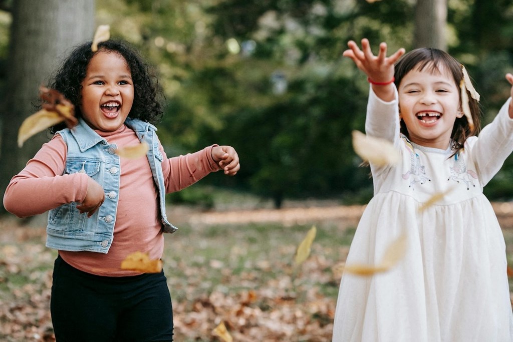 two young girls playing outside and tossing autumn leaves in the air