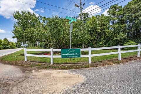 a white fence and a green sign on the side of a road