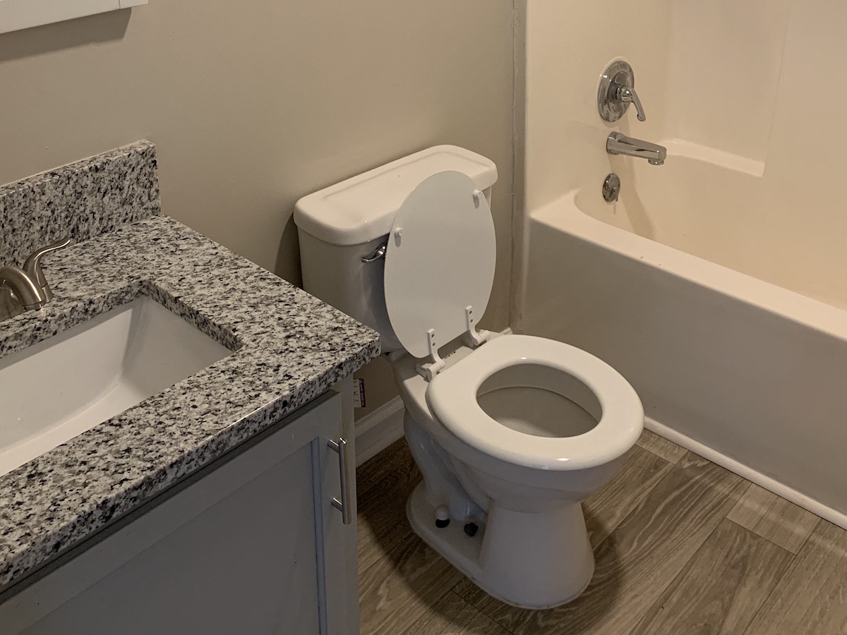 Bathroom with granite countertop, plank style flooring, toilet, and tub /shower