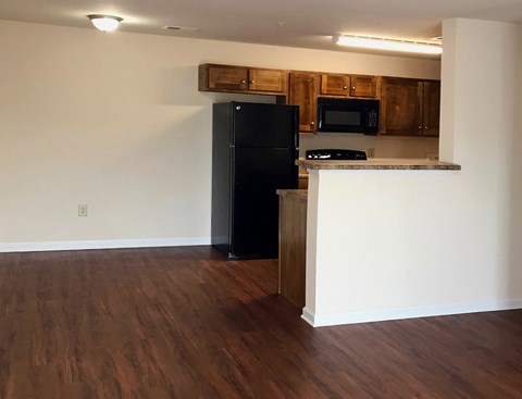 an empty living room with a refrigerator and a kitchen